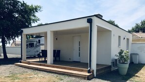 Un espace extérieur abrité, doté d’une terrasse en bois, d’un coin salon et d’une plante en pot.