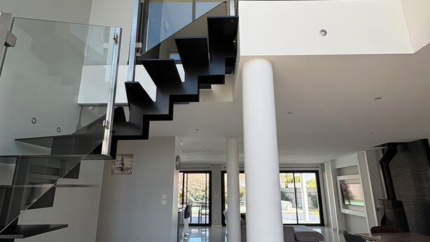 Un intérieur moderne avec un escalier en verre, un coin repas et une vue sur l’extérieur.