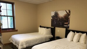 Una habitación de hotel con dos camas individuales, una ventana con persianas, un cuadro en la pared y una mesita entre las camas.