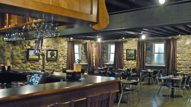 Un interior de restaurante con paredes de piedra, mostrador de bar de madera y varias mesas y sillas.