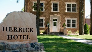 Un letrero de piedra con la inscripción "HERRICK HOTEL", ubicado frente a un edificio de ladrillo con varias ventanas y una puerta.