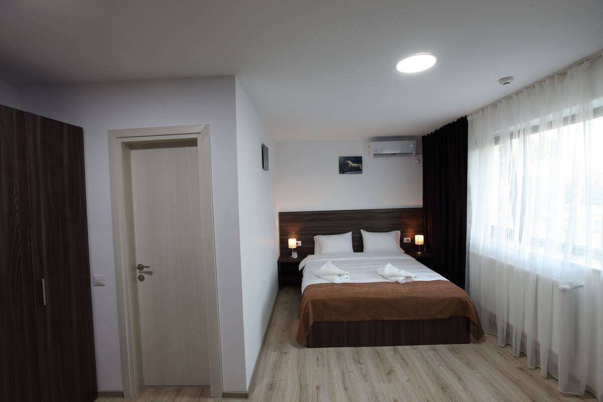 Habitació d'hotel amb un llit, una vetusta, una porta i una finestra amb cortines.