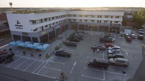 A parking lot with multiple cars and a few people. There is a strip mall with a Bliss Hotel and a GC Gold Club. - Bliss Inn Tunari (Tunari)