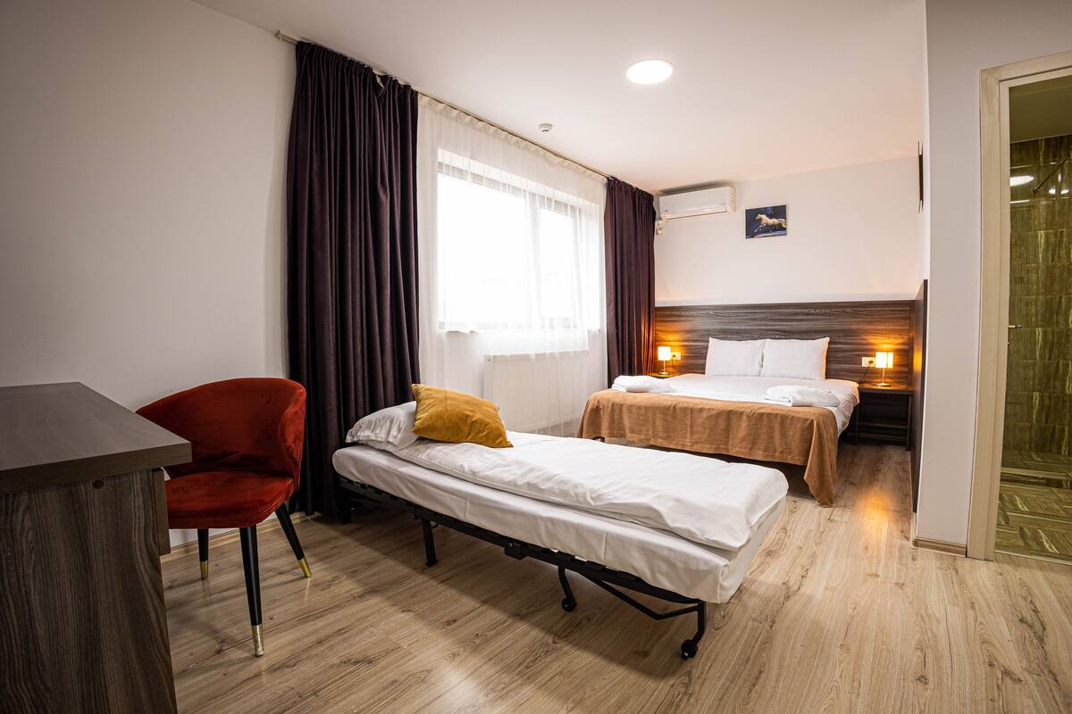Habitació d'hotel amb dos llits individuals, un escriptori de fusta, una cadira vermella i una finestra amb cortines.