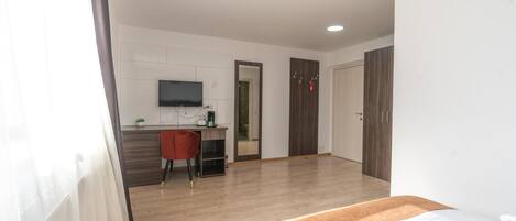Una habitación de hotel con cama, escritorio, silla, televisor y armario.