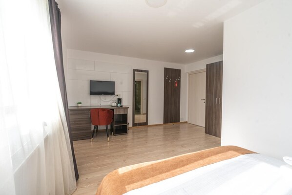 A hotel room with a bed, a desk, a chair, a TV, and a wardrobe.