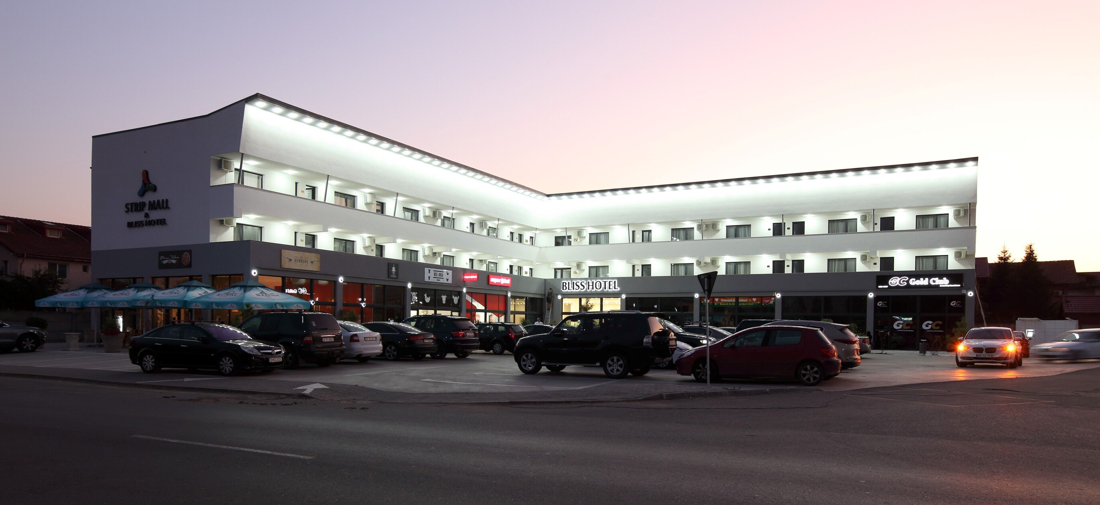 A multi-story hotel with a flat facade, multiple balconies, and a row of shops on the ground floor.