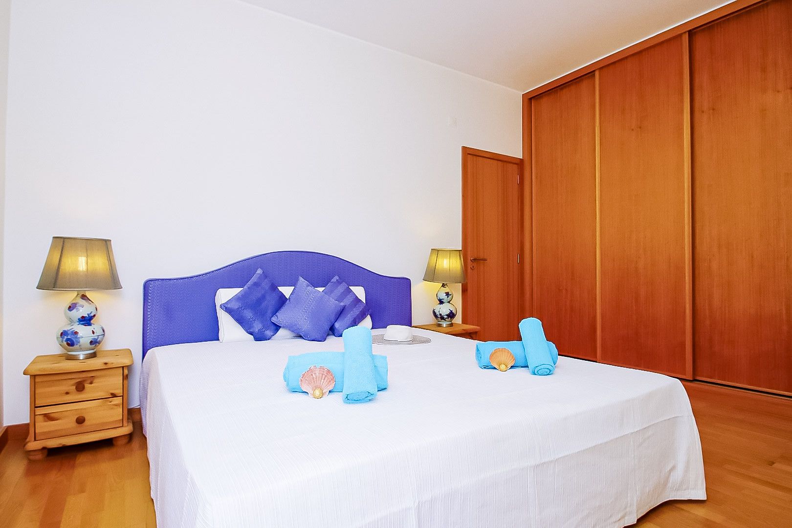 A bedroom with a bed, two bedside tables, a wooden wardrobe, and a nightstand.