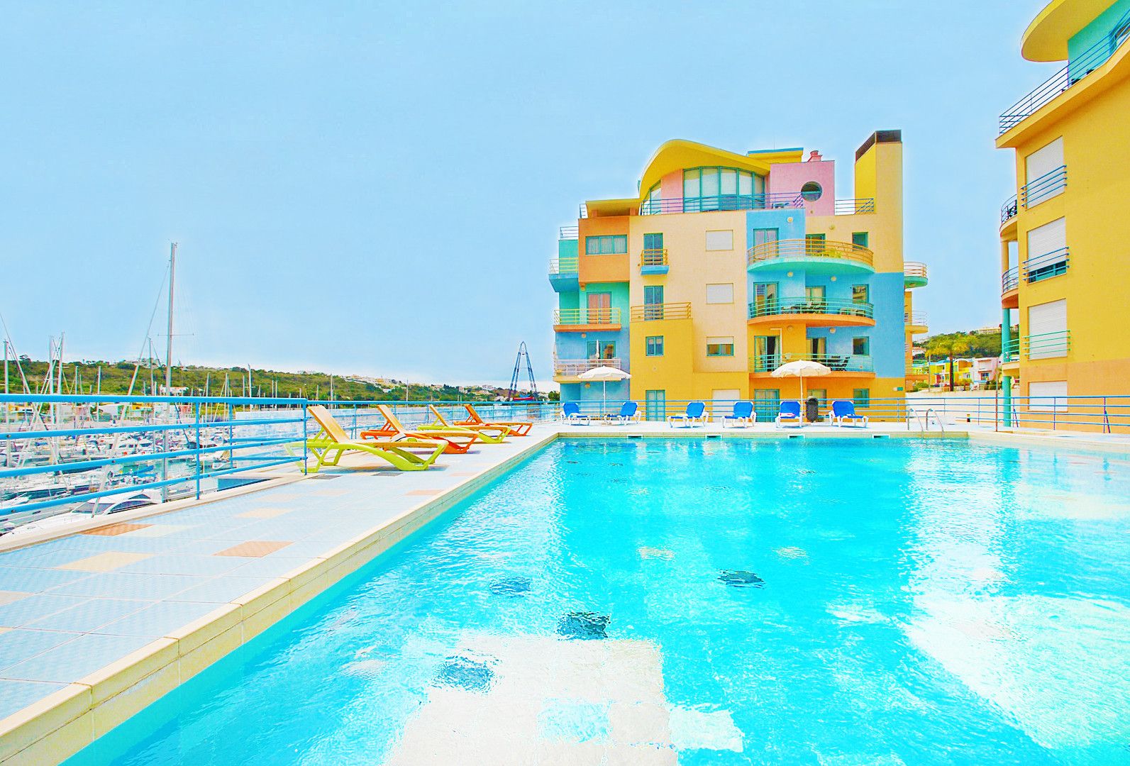 A swimming pool with lounge chairs and a multi-story building with balconies.