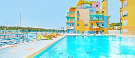 A swimming pool with lounge chairs and a multi-story building with balconies.