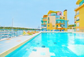 Une piscine avec des chaises longues et un immeuble à plusieurs étages doté de balcons.