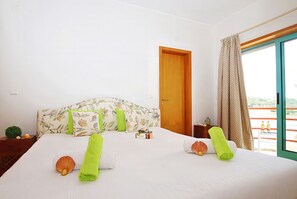 A hotel room with a bed, a wooden door, a window with curtains, and a small table with bottles.