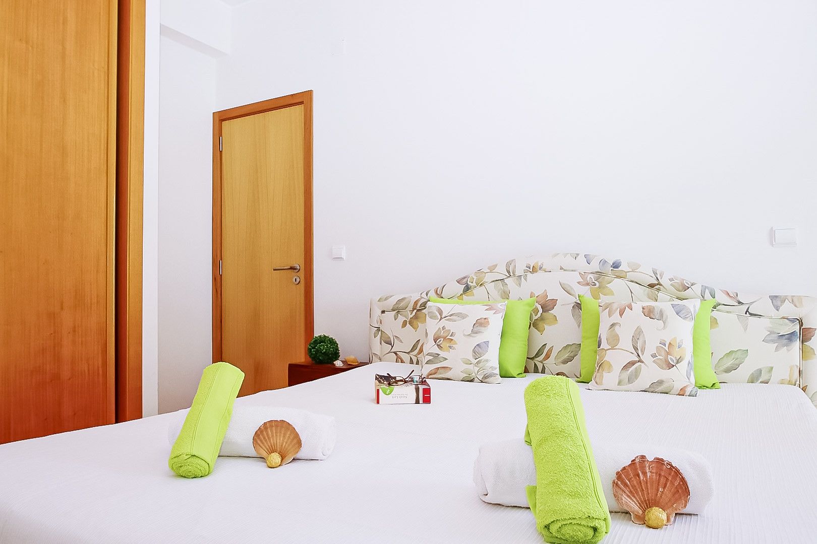 A hotel room with a bed, a wooden door, and a floral headboard.