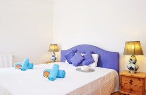 Una cama bien hecha con toallas azules y una concha marina, dos lámparas de noche, una mesita de noche de madera y un radiador blanco.