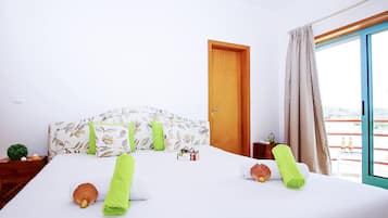 A hotel room with a bed, a wooden door, a window with curtains, and a small table with a plant.