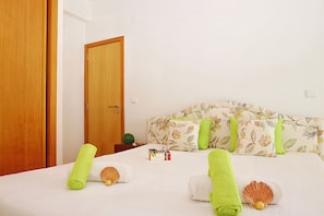 A hotel room with a bed, a wooden door, a nightstand, and a small potted plant.