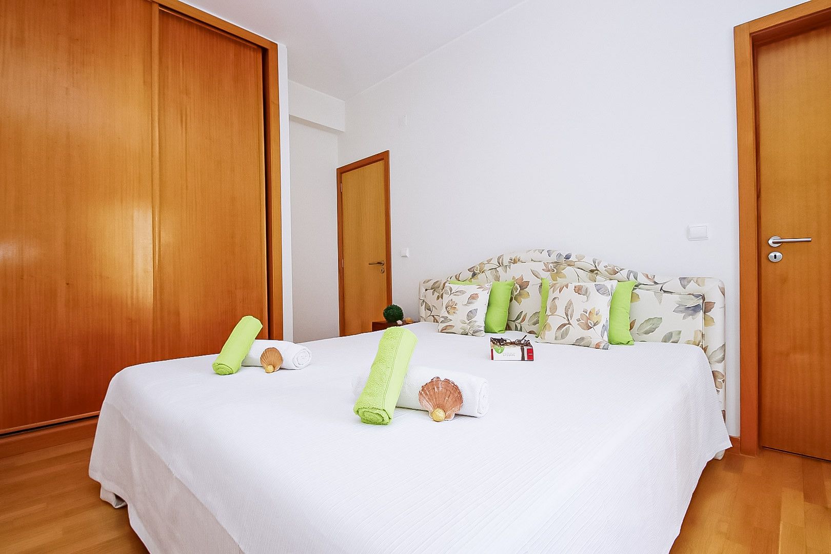 A hotel room with a bed, wooden doors, a floral headboard, and a small nightstand with a lamp.