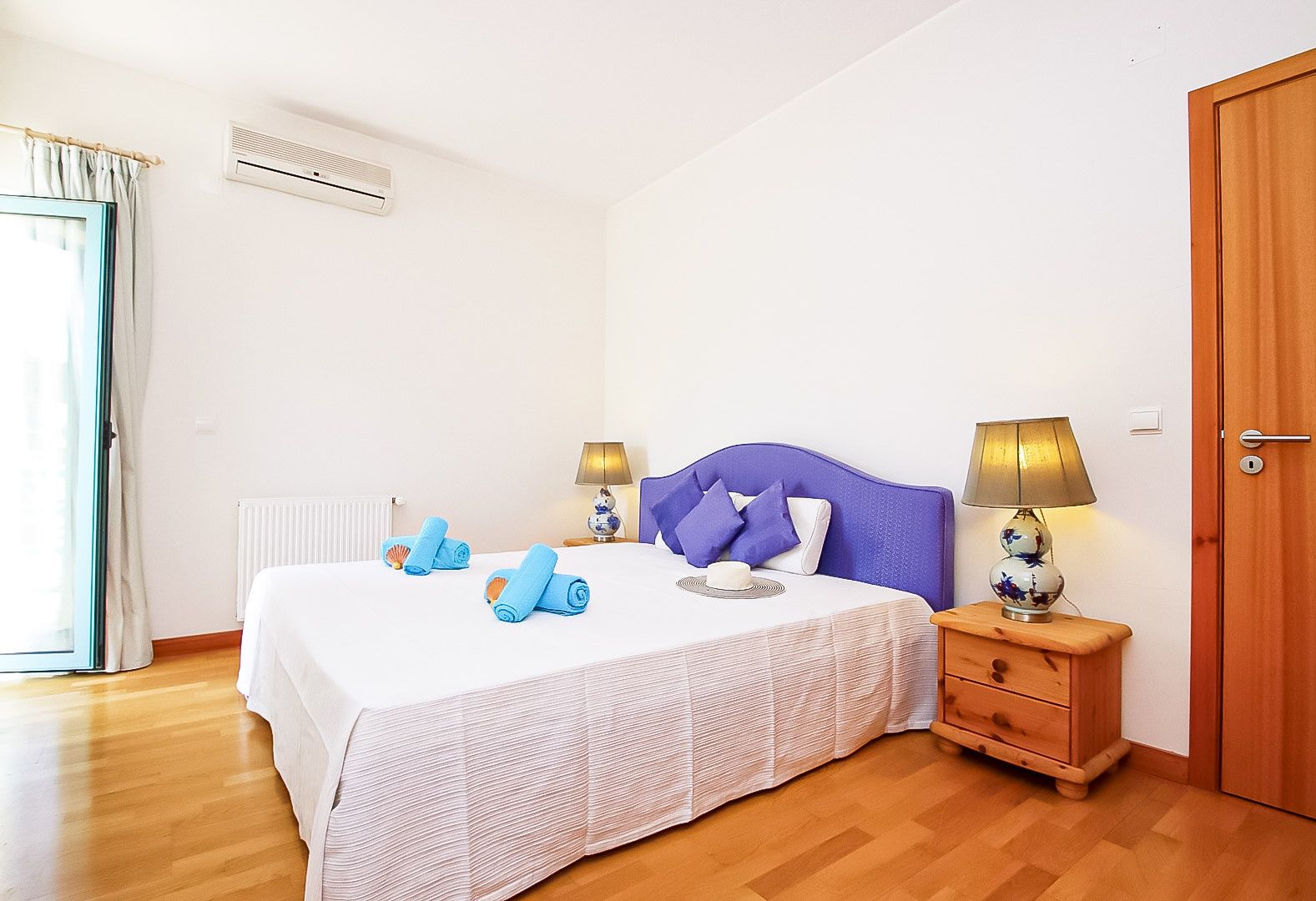 A bedroom with a bed, bedside tables, a lamp, a door, and a window with curtains.