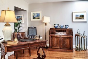 A wooden desk with a lamp, a vintage telephone, and a framed picture on the wall.