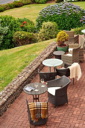 Une terrasse extérieure aménagée avec des meubles en osier, des murs en pierre et une variété de plantes.