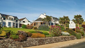 A row of modern, two-story houses with a landscaped garden in front, a stone wall, and a sign indicating 'Greenmount Houses'. - Greenmount House (Dingle)