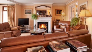 A living room with leather sofas, a fireplace, a television, and books. - Greenmount House (Dingle)