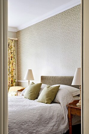 Un lit bien fait, recouvert d’une courtepointe blanche et agrémenté de deux coussins verts, avec deux lampes de chevet placées de part et d’autre sur des tables de nuit en bois.