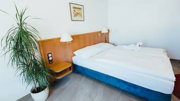 Ein Hotelzimmer mit Bett, Topfpflanze, Nachttisch und Wandlampe.