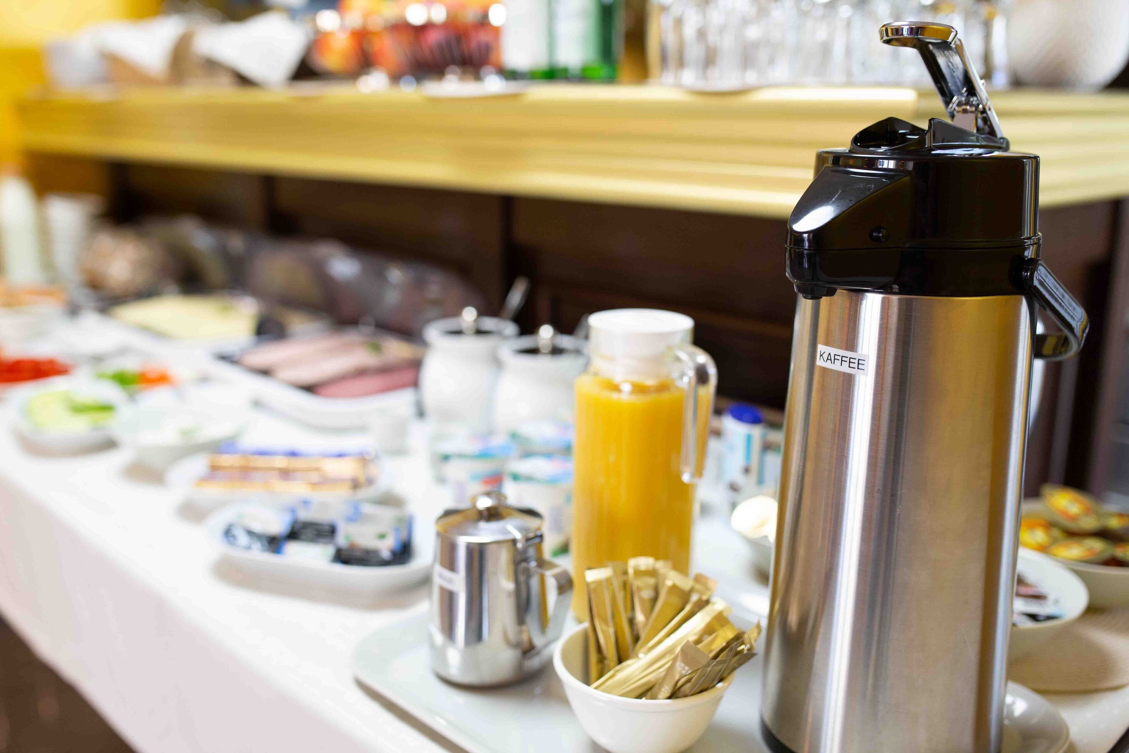 A buffet setup with various food items, a coffee maker, and a thermos.
