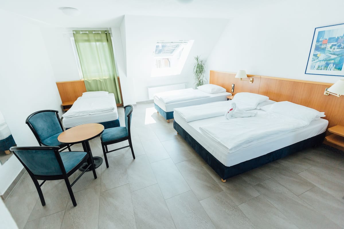 Une chambre d’hôtel avec deux lits, une petite table, deux chaises, une fenêtre donnant sur un beau paysage et un tableau au mur.
