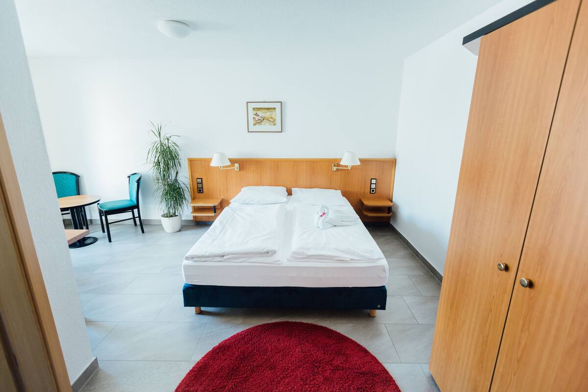Une chambre d’hôtel avec un lit, des tables de chevet, un bureau, une chaise et une plante en pot.