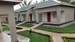 A row of modern buildings with flat roofs, a central courtyard with manicured grass and pathways, and a small tree in the middle. - Delight Lodge (Blantyre)