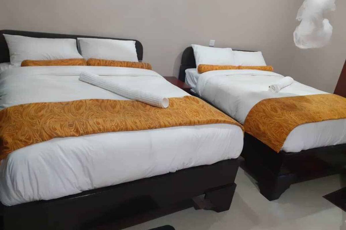 A hotel room with two beds, each with white bedding and orange throw pillows.