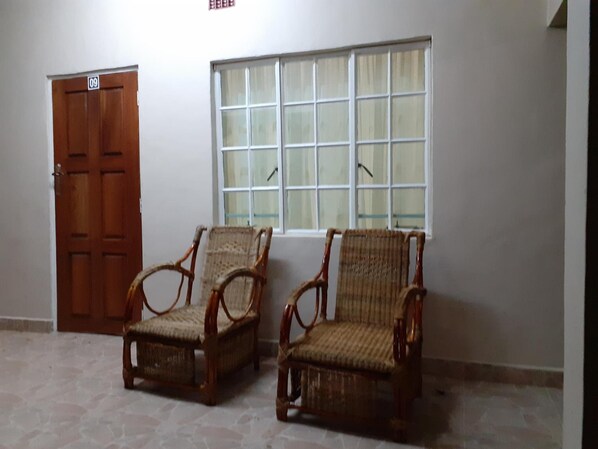A room with two wicker chairs, a wooden door, and a window with a view.