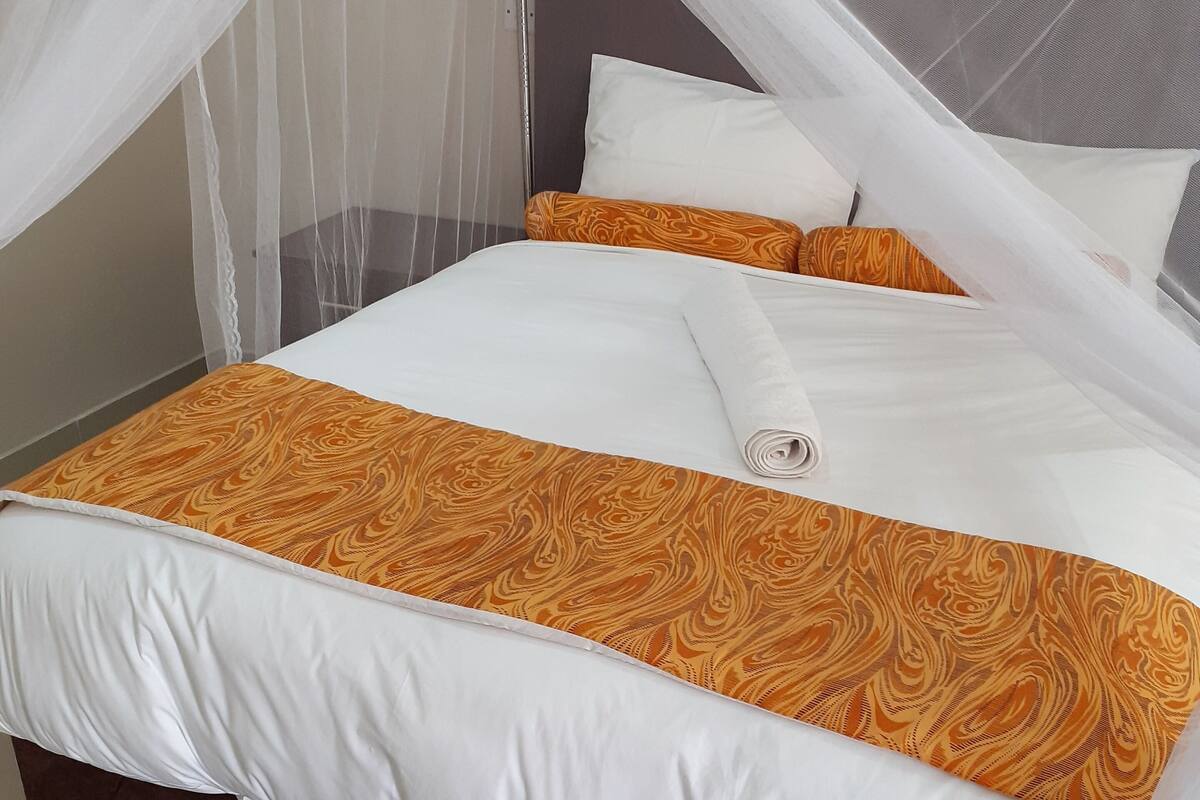 A neatly made bed with a white and orange patterned bedspread, white pillows, and a brown upholstered headboard.