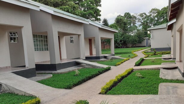 A modern building with a symmetrical design, featuring a central pathway flanked by neatly trimmed grass and small shrubs. - Delight Lodge (Blantyre)