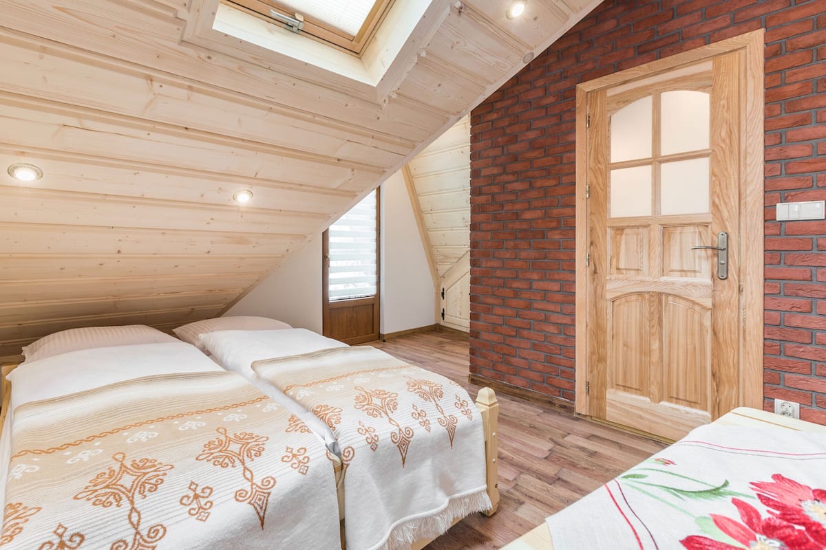 A bedroom with two beds, a skylight, a wooden door, and a brick wall.