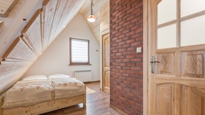 Un dormitorio con techo inclinado, una cama de madera, pared de ladrillo y una puerta de madera.