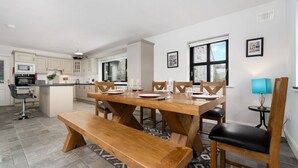 A modern kitchen with a dining area, featuring a wooden table and bench, and a small island with a sink. - Cottage 345 - Oughterard  - sleeps 10 guests  in 4 bedrooms (Oughterard)