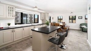 A modern kitchen with a central island, bar stools, and a dining area with a wooden table and chairs. - Cottage 345 - Oughterard  - sleeps 10 guests  in 4 bedrooms (Oughterard)