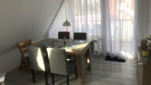 Zona pranzo con tavolo in legno, quattro sedie, lampada a sospensione e tende leggere.
