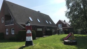 Un edificio residenziale con tetto a falde, un piccolo giardino e un’area giochi con uno scivolo.