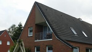 Una casa a due piani con tetto spiovente, un balcone visibile al secondo piano e un camino.