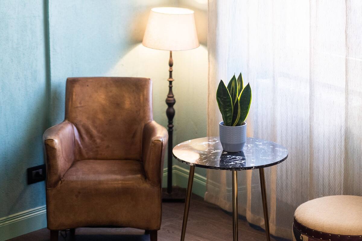 A room with a brown leather armchair, a small round table with a lamp and a potted plant, and a pink electric guitar on the wall.