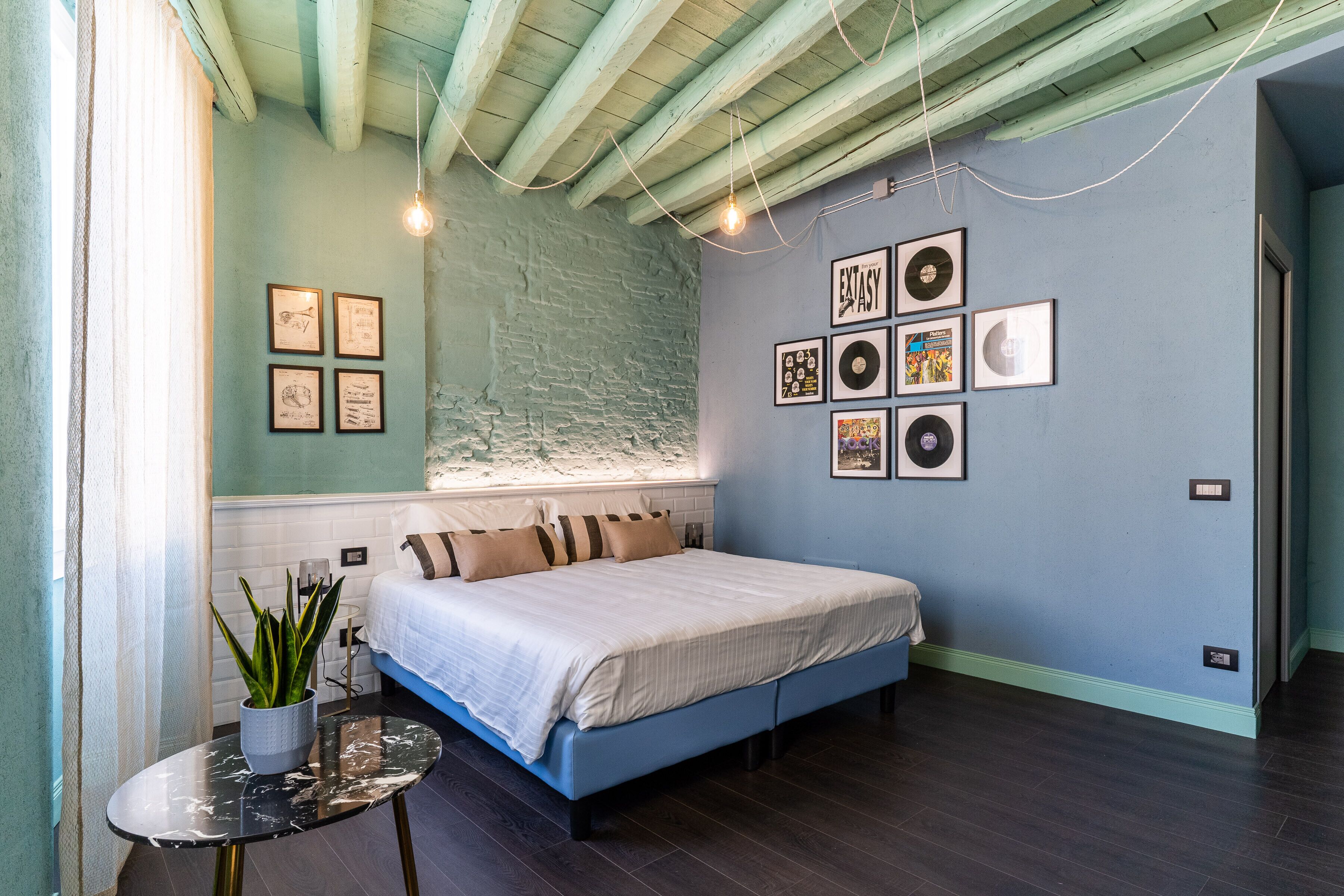 A bedroom with a bed, a small table with a plant, and framed pictures on the wall.