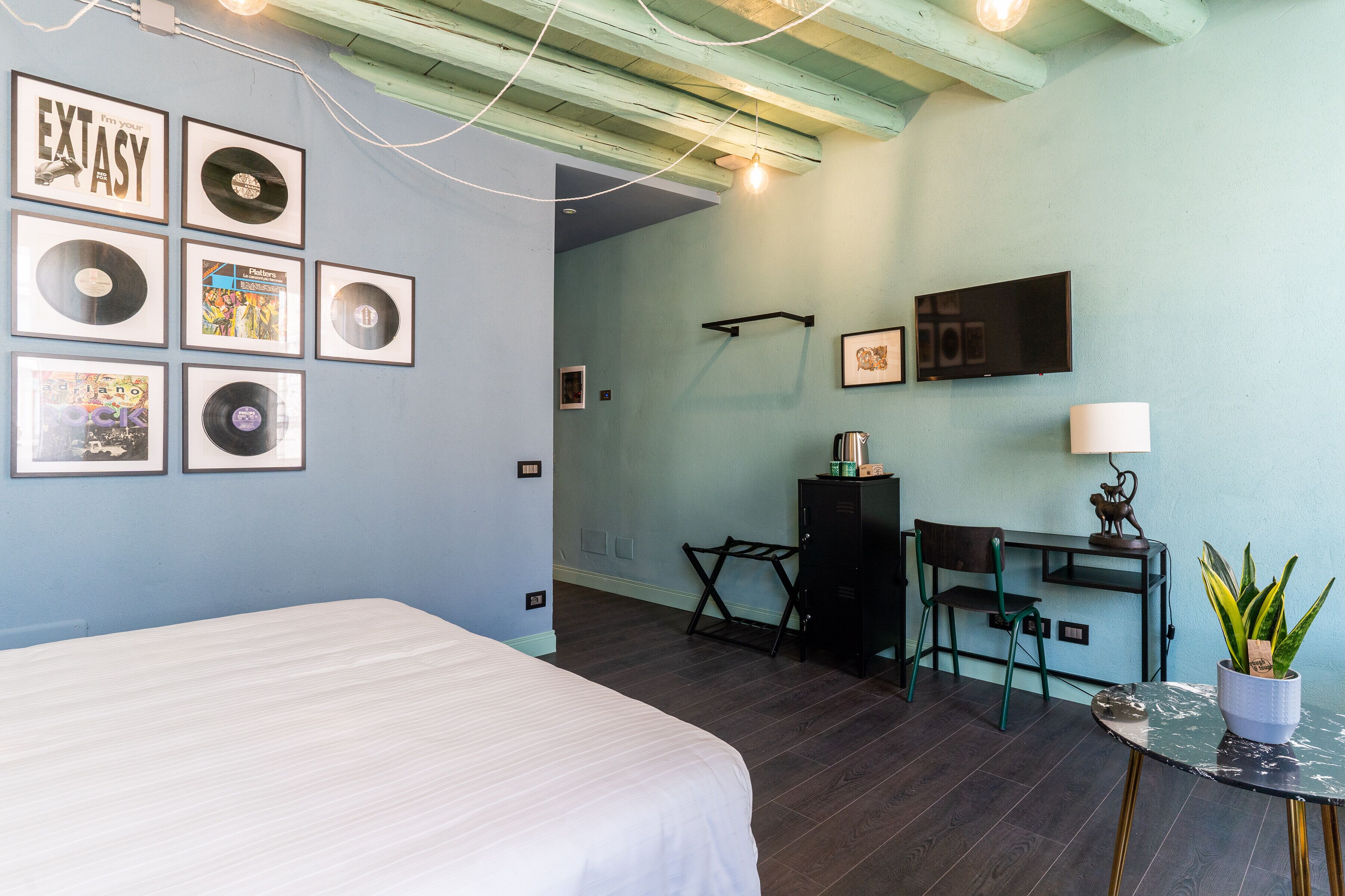 Une pièce comprenant un lit, un bureau, une chaise, un téléviseur et des pochettes de disques encadrées accrochées au mur.