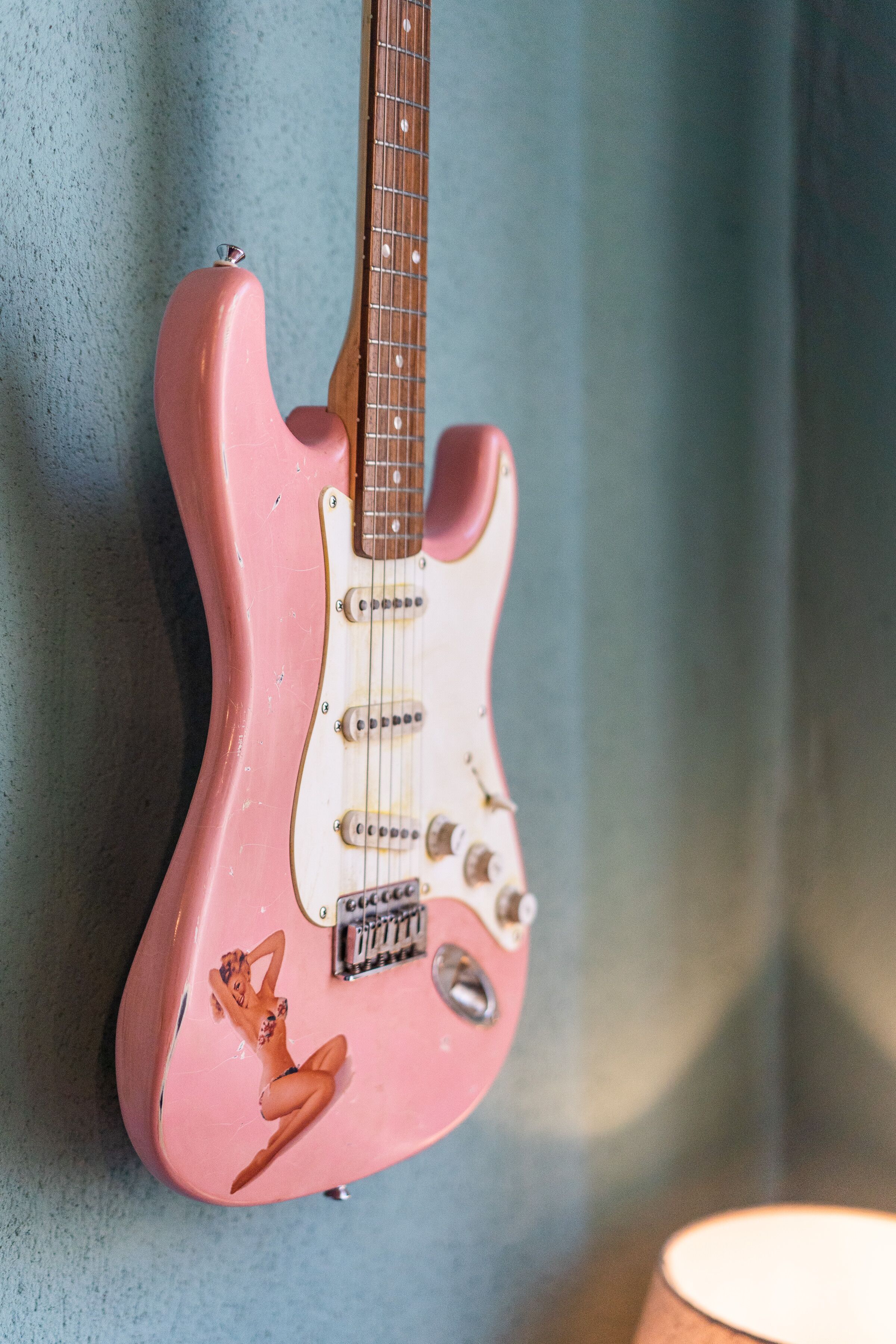 Eine pinkfarbene elektrische Gitarre mit einem dekorativen Frosch-Aufkleber, an einer Wand angebracht.