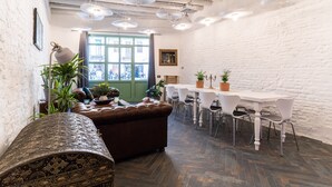 Ein modernes Interieur mit Fischgrätparkett, weißen Backsteinwänden, einem Essbereich mit weißem Tisch und Stühlen sowie einem braunen Ledersofa.