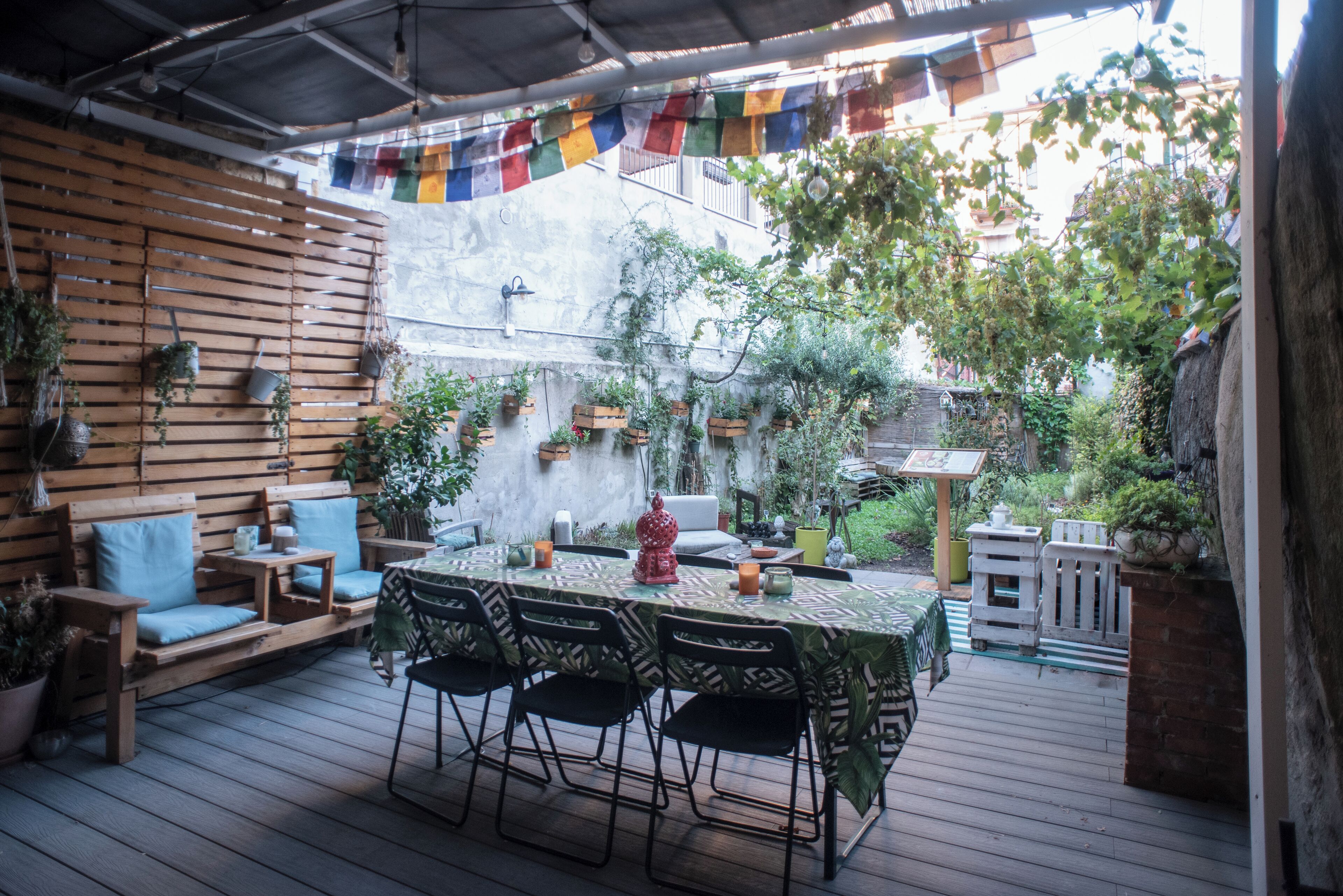 An outdoor patio with a wooden deck, a table set for dining, and various potted plants.