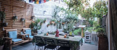 An outdoor patio with a wooden deck, a table set for dining, and various potted plants.